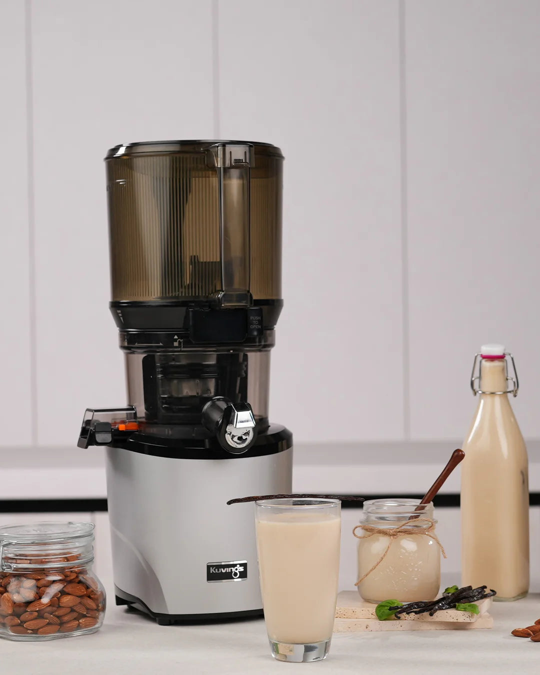 Kuvings AUTO10 slow juicer with vegan almond milk, almonds, vanilla and homemade plant-based milk bottles.