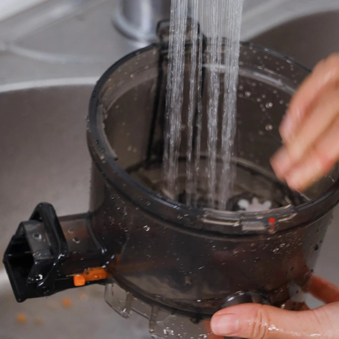 Kuvings AUTO10S slow juicer juicing drum being rinsed under running water for easy cleaning after juicing.