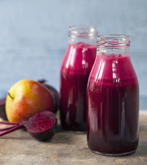 Two bottles of beetroot juice with a background of apples and beets.