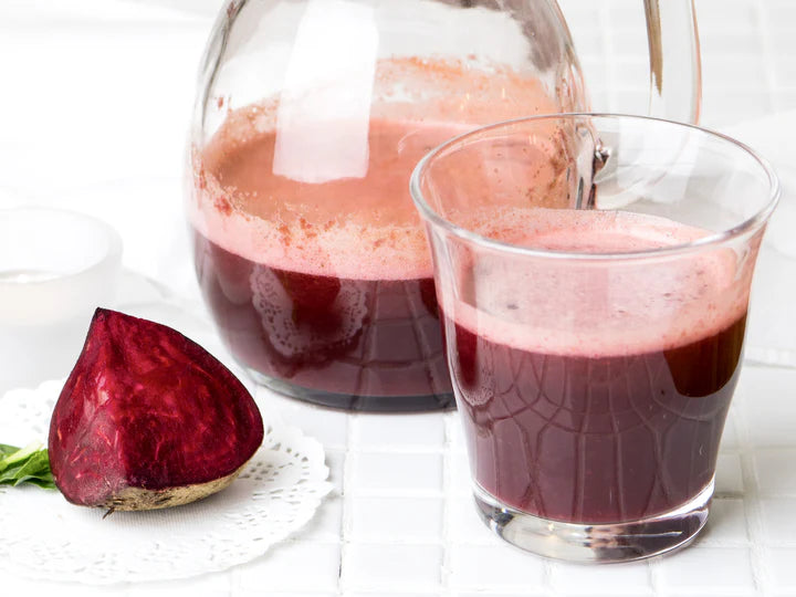 Glass of beet juice with a whole beet on a white surface