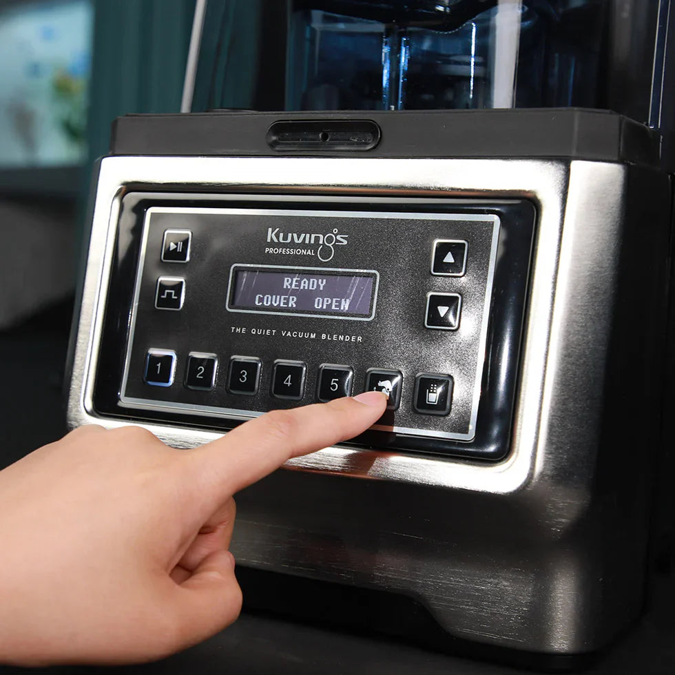 Angled close-up view of a hand pressing a function button on the silver metallic control panel of a Kuvings CB1000 Professional Quiet Vacuum Blender, showing the digital display text 'READY COVER OPEN'.