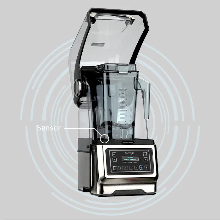 Widok z przodu pod kątem, profesjonalny blender próżniowy Kuvings CB1000 z otwartą przezroczystą osłoną wyciszającą, z grafiką etykiety wskazującą na wbudowany czujnik bezpieczeństwa na szarym tle z koncentrycznymi okręgami.