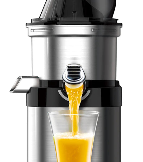 Frontale Nahaufnahme-Studioaufnahme des oberen Trommelbereichs eines gebürsteten Edelstahl-Kuvings Chef CS700 gewerblichen Slow Juicers mit geöffneter Chrom-Smart-Cap, der frischen Orangensaft in ein Glas gießt, vor einem weißen Hintergrund.
