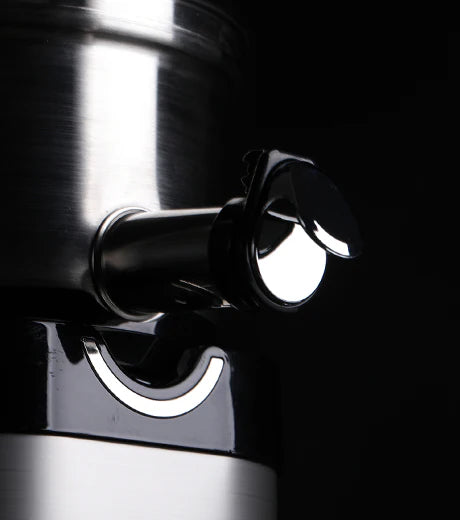 Dreiviertel-Nahaufnahme-Studio-Produktaufnahme des Saftauslasses aus Edelstahl und der chromakzentuierten Smart Cap eines Kuvings Chef CS700 gewerblichen Slow Juicers, dramatisch beleuchtet vor einem einfarbigen schwarzen Hintergrund.