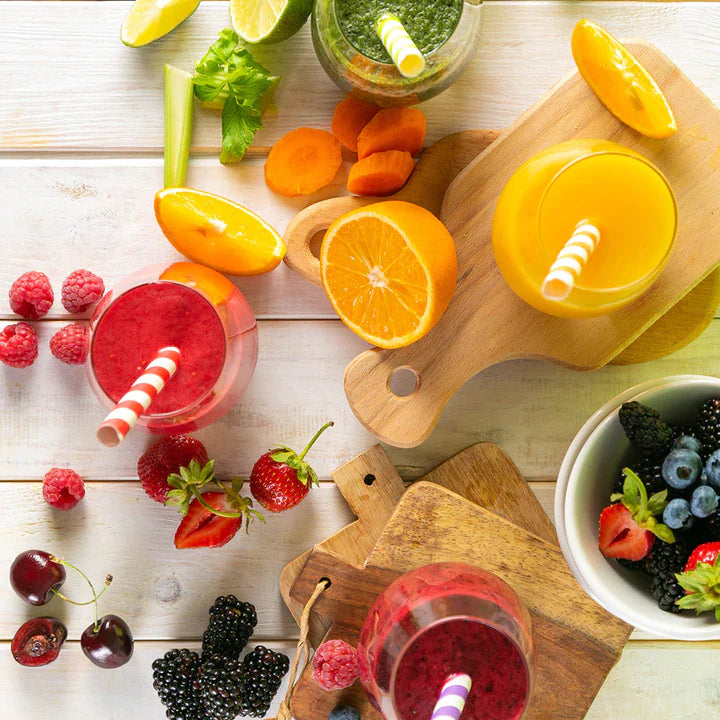 Assorted fresh fruits, vegetables, and smoothie glasses on a wooden surface.