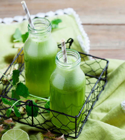 Two green smoothies in glass jars with straws on a green cloth.