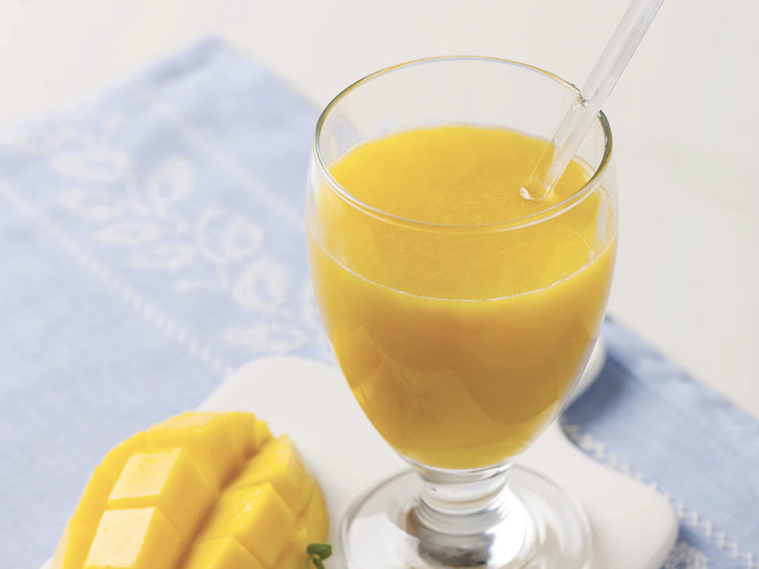 Glass of mango juice with a slice of mango on a light blue cloth