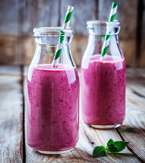 Two glass bottles filled with pink smoothie on a wooden surface.