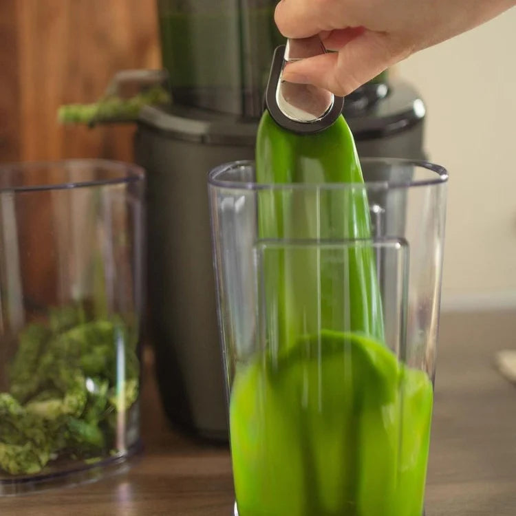 Kuvings kitchen juicer used with a glass container with a blender in the background for healthy homemade juice and smoothie preparation.